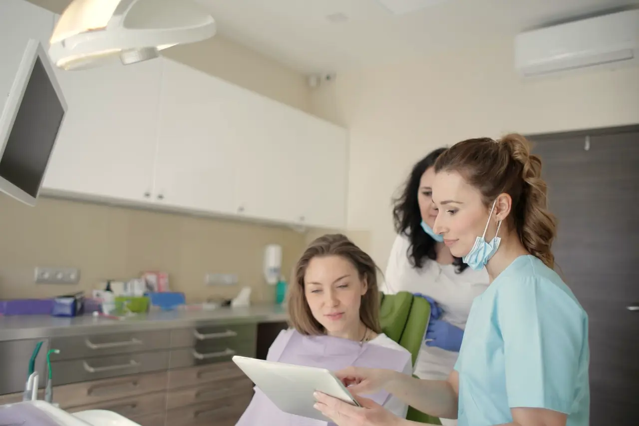 A dental hygienist shows a patient a tablet while a colleague looks on, in a warm, bright treatment room (stock photo, not this practice)